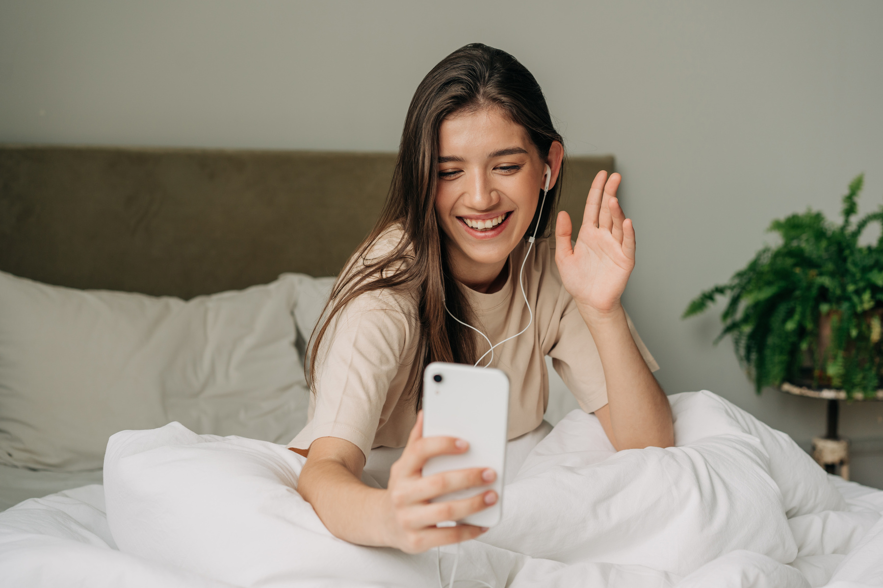 Woman Sitting on Bed after Waking up and Talking on Video Call Using Mobile Phone and Headphones